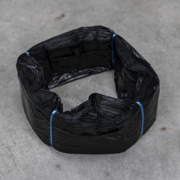 Fascio di sacchetti in plastica nera, legati con filo blu, disposti a forma di anello su una superficie grigia