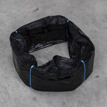 Fascio di sacchetti in plastica nera, legati con filo blu, disposti a forma di anello su una superficie grigia