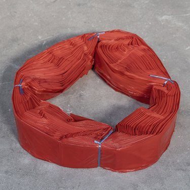 Fascio di sacchetti in plastica rossa XL, legati con filo blu, disposti a forma di anello su una superficie grigia