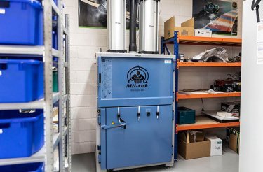 Pressa a balle Mil-tek A406 installata nel magazzino di Skjern Motorcycles, affiancata da scaffali con componenti e ricambi